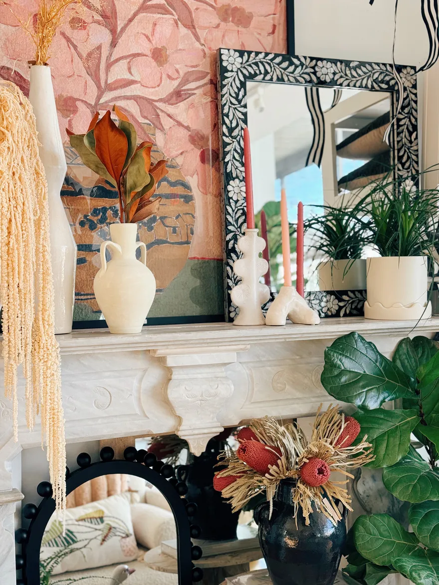 A marble mantel styled with cream amphora vases, dried florals and coral taper candles.